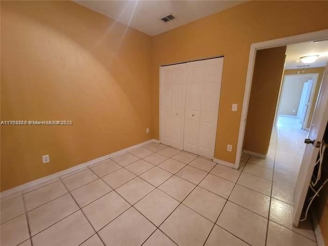 unfurnished bedroom featuring light tile patterned floors, a closet, visible vents, and baseboards