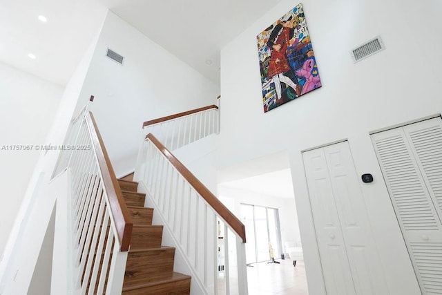 stairs with a high ceiling, wood finished floors, and visible vents