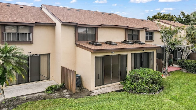 back of property with stucco siding, a patio, a lawn, and roof with shingles