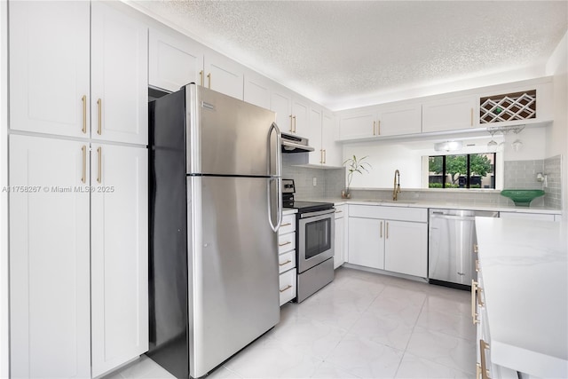 kitchen featuring under cabinet range hood, stainless steel appliances, a sink, white cabinetry, and decorative backsplash