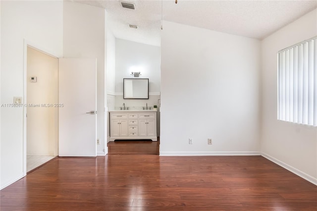 interior space featuring baseboards, visible vents, ensuite bath, dark wood-style flooring, and a textured ceiling