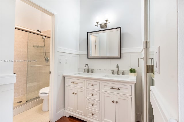 bathroom with a stall shower, a sink, toilet, and double vanity