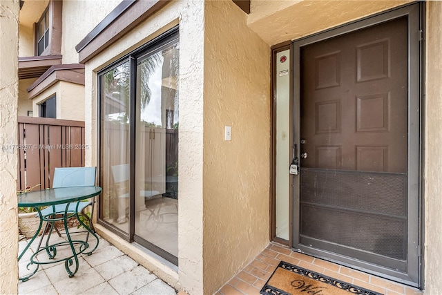 view of exterior entry with fence and stucco siding