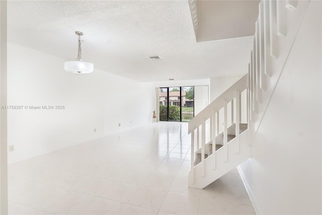 unfurnished room with baseboards, visible vents, stairway, and a textured ceiling