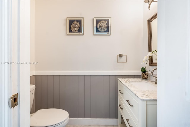 half bath featuring toilet, vanity, and wainscoting