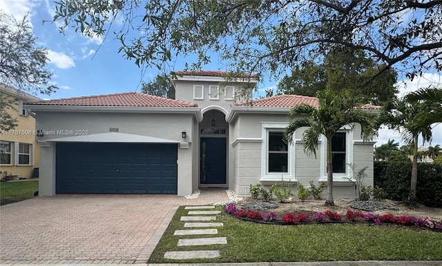 mediterranean / spanish home with a tile roof, an attached garage, decorative driveway, a front lawn, and stucco siding