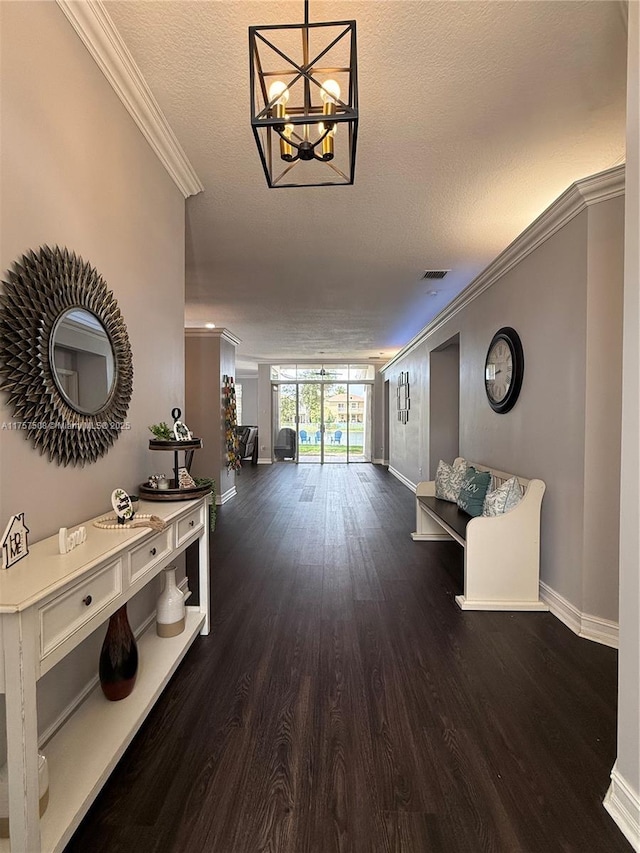 hallway with a notable chandelier, dark wood-style flooring, visible vents, baseboards, and crown molding