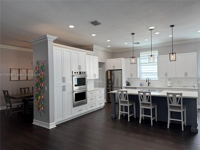 kitchen featuring visible vents, light countertops, appliances with stainless steel finishes, a kitchen bar, and dark wood finished floors