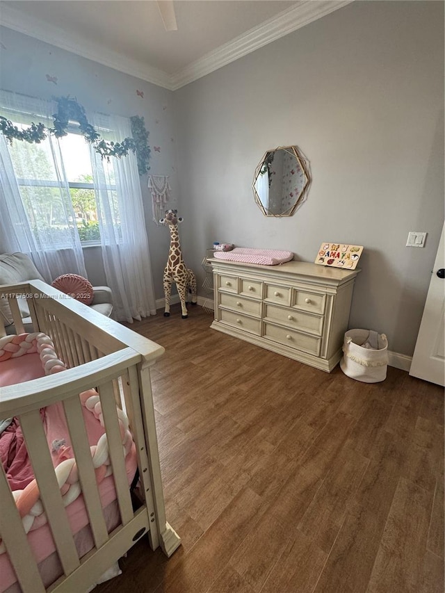 unfurnished bedroom featuring a nursery area, crown molding, baseboards, and wood finished floors