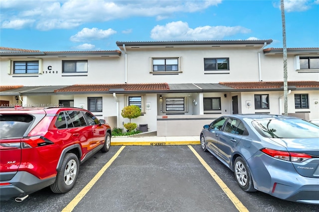 townhome / multi-family property featuring uncovered parking, a tiled roof, and stucco siding