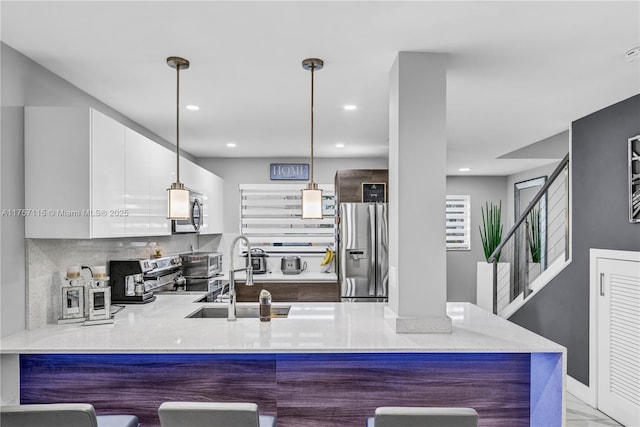 kitchen featuring modern cabinets, appliances with stainless steel finishes, a peninsula, a kitchen bar, and a sink