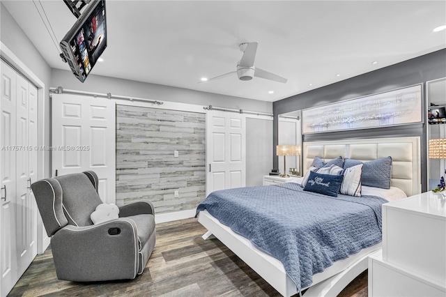 bedroom with ceiling fan, a barn door, recessed lighting, wood finished floors, and a closet