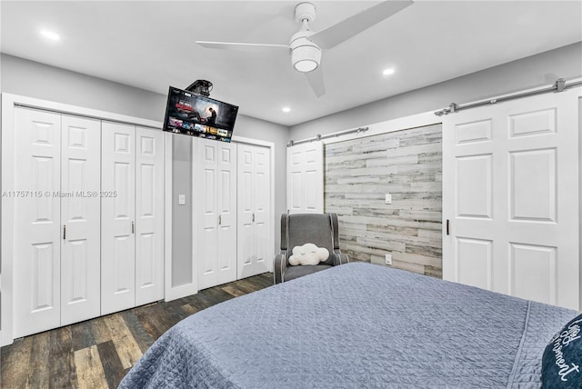 bedroom with a barn door, a ceiling fan, wood finished floors, multiple closets, and recessed lighting