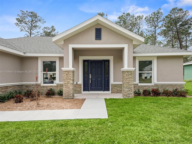 entrance to property with stone siding, roof with shingles, a lawn, and stucco siding