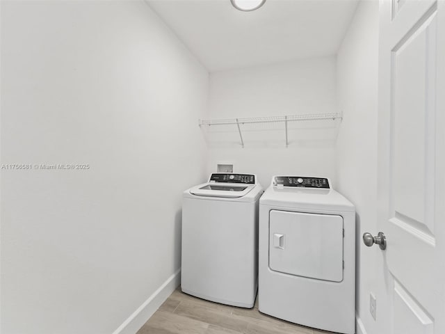 clothes washing area with laundry area, washing machine and dryer, baseboards, and light wood-style floors