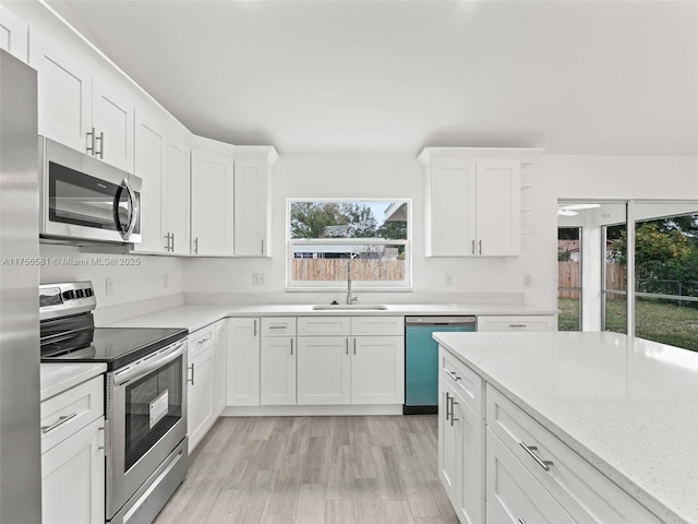 kitchen featuring light wood finished floors, white cabinetry, appliances with stainless steel finishes, and a sink