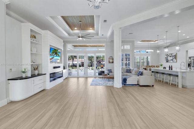 living area with light wood-style floors, a tray ceiling, french doors, and crown molding