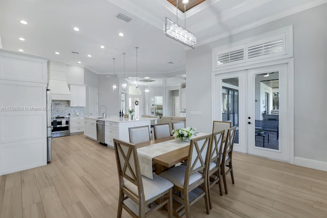 dining space with light wood-style flooring, ornamental molding, and french doors