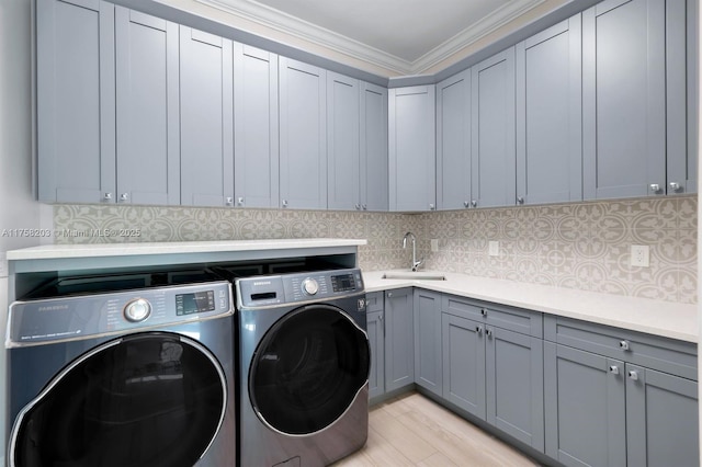 washroom featuring cabinet space, light wood-style flooring, ornamental molding, a sink, and independent washer and dryer