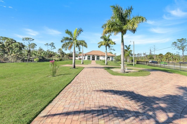 view of community with fence, decorative driveway, and a yard