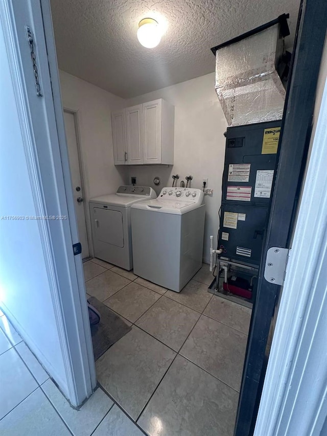 clothes washing area featuring light tile patterned floors, a textured ceiling, washing machine and clothes dryer, and cabinet space