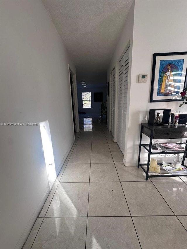 corridor featuring light tile patterned floors, baseboards, and a textured ceiling