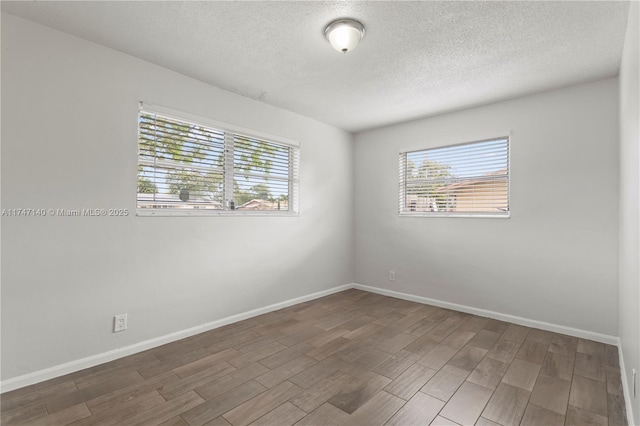 empty room with a textured ceiling, baseboards, and wood finished floors