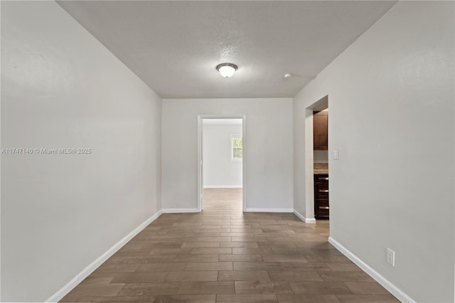 unfurnished room with a textured ceiling, dark wood-type flooring, and baseboards