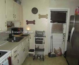 kitchen featuring a wall unit AC, light countertops, light tile patterned flooring, a sink, and stainless steel fridge