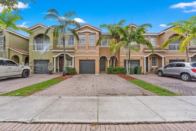 townhome / multi-family property with driveway, a tile roof, a garage, and stucco siding