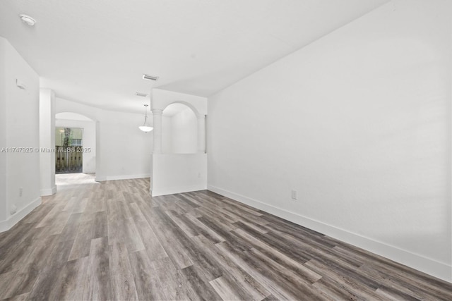 unfurnished room with baseboards, visible vents, arched walkways, and wood finished floors