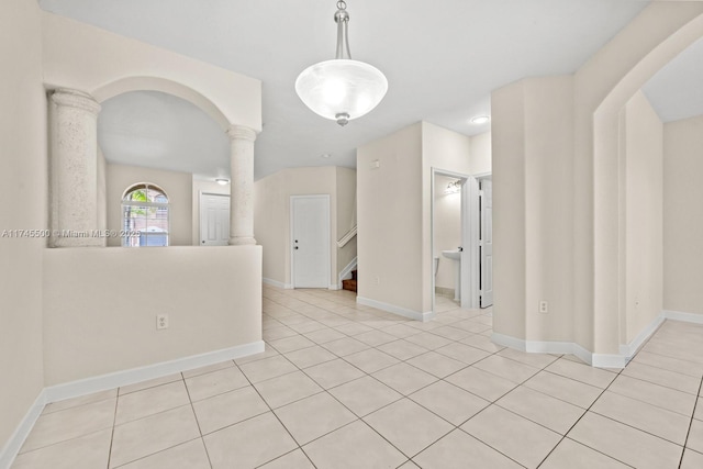 unfurnished room with light tile patterned floors, decorative columns, baseboards, arched walkways, and stairway