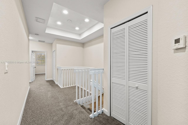 corridor featuring carpet floors, baseboards, a raised ceiling, and an upstairs landing