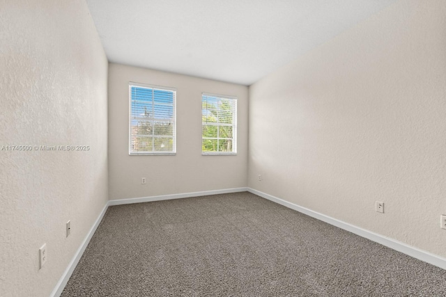 empty room featuring carpet floors, a textured wall, and baseboards