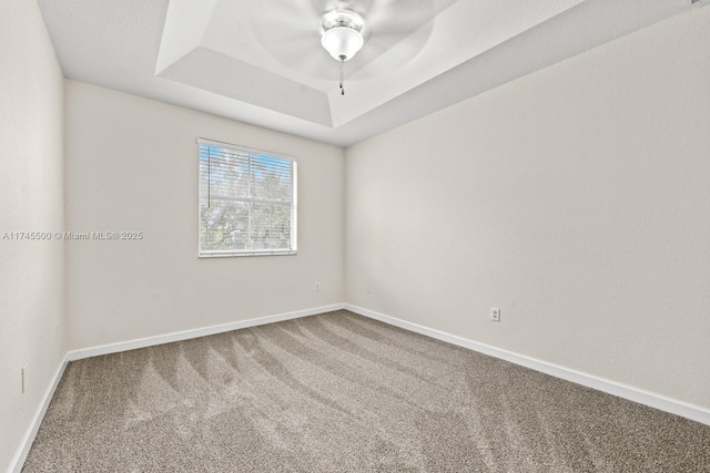 carpeted spare room with baseboards and a tray ceiling