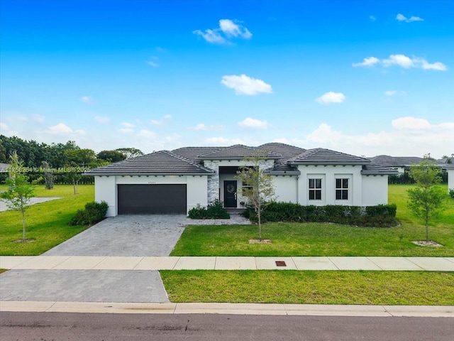 prairie-style house with an attached garage, a tile roof, decorative driveway, stucco siding, and a front lawn