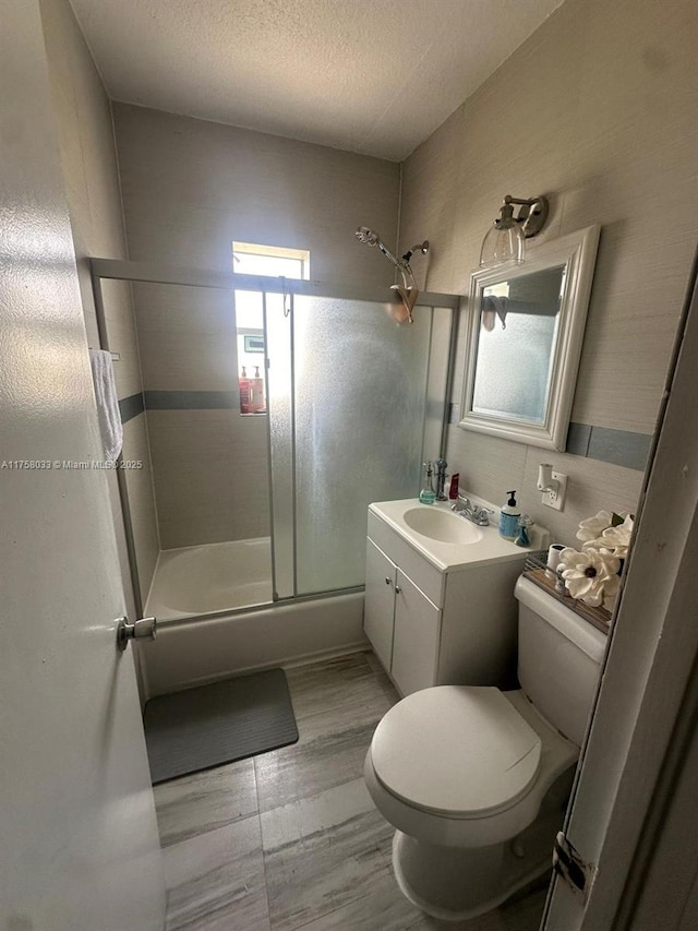 bathroom with toilet, wood finished floors, combined bath / shower with glass door, a textured ceiling, and vanity