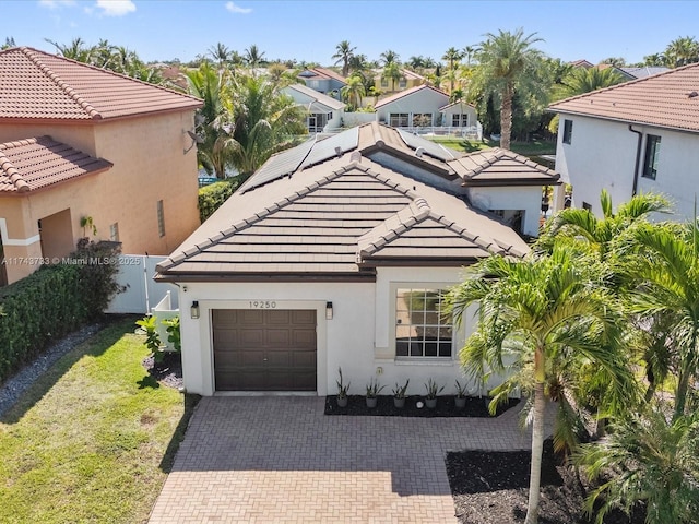 mediterranean / spanish house featuring a garage, a tile roof, fence, decorative driveway, and a front yard