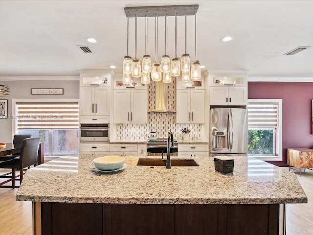 kitchen with crown molding, backsplash, appliances with stainless steel finishes, a sink, and wall chimney exhaust hood