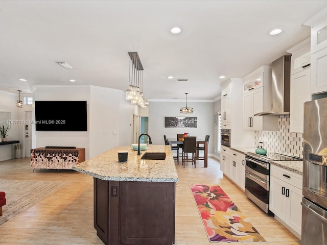 kitchen featuring a sink, appliances with stainless steel finishes, wall chimney range hood, an island with sink, and crown molding