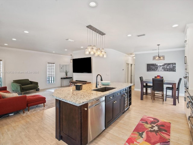 kitchen with hanging light fixtures, stainless steel dishwasher, open floor plan, a sink, and light wood-type flooring