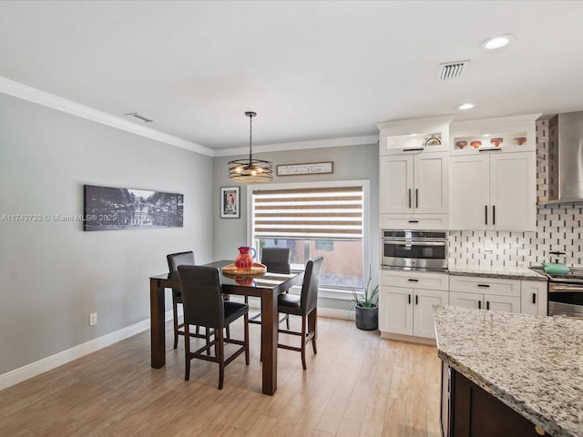 dining room with baseboards, light wood finished floors, visible vents, and crown molding