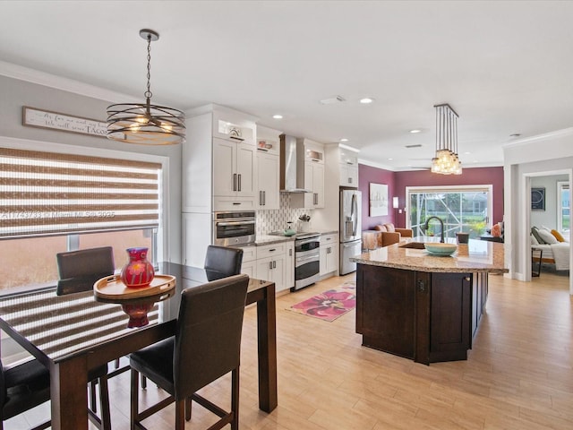 kitchen with a sink, light wood-style floors, white cabinets, appliances with stainless steel finishes, and wall chimney exhaust hood