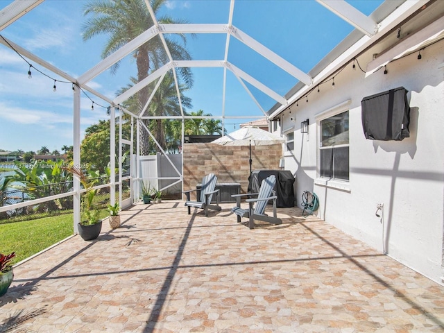 view of patio featuring glass enclosure, a grill, and fence