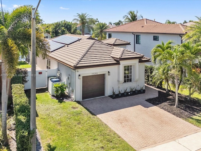 mediterranean / spanish home featuring decorative driveway, a tile roof, an attached garage, a front yard, and fence