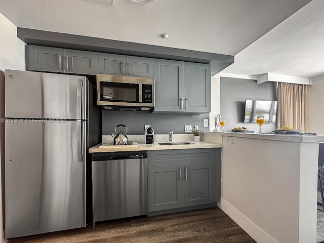 kitchen featuring appliances with stainless steel finishes, a peninsula, gray cabinets, light countertops, and a sink