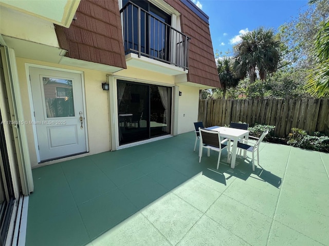 view of patio with a balcony, fence, and outdoor dining space