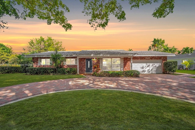 ranch-style home featuring an attached garage, brick siding, decorative driveway, and a front yard