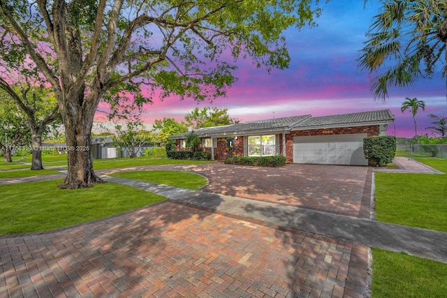 ranch-style house with decorative driveway, a lawn, an attached garage, fence, and a tiled roof