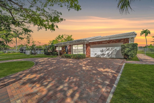 ranch-style house with a lawn, an attached garage, fence, decorative driveway, and brick siding